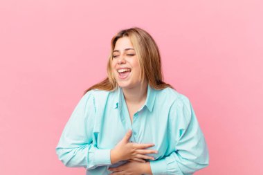 Kıvrımlı, güzel, sarışın kadın komik bir şakaya yüksek sesle gülüyor.