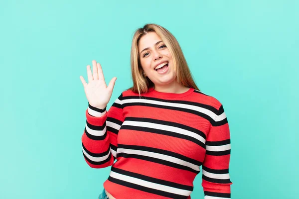 Curvy pretty blonde woman smiling happily, waving hand, welcoming and greeting you — Stock Image Curvy Pretty Blonde Woman Smiling Happily Waving Hand Welcoming Greeting Royalty Free Stock Photos