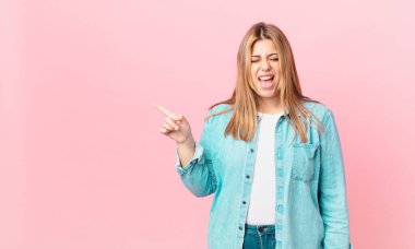 Kıvrımlı, güzel sarışın kadın agresif bir şekilde bağırıyor, çok kızgın görünüyor.