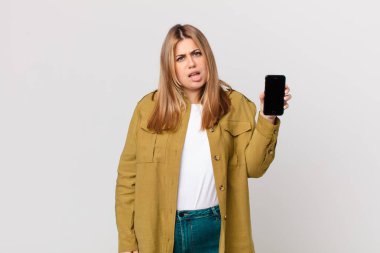 Kıvrımlı, güzel sarışın kadın kafası karışık ve akıllı bir telefon tutuyor.