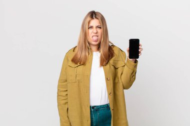 Kıvrımlı, güzel, sarışın bir kadın. Tiksinmiş ve rahatsız olmuş hissediyor. Dilini dışarı çıkarıyor ve akıllı bir telefon tutuyor.