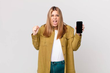 kıvrımlı, güzel, sarışın bir kadın sinirli bir ifadeyle bağırıyor ve elinde akıllı bir telefon tutuyor.