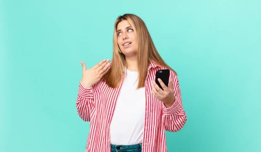 kıvrımlı, güzel, sarışın kadın stresli, endişeli, yorgun ve hayal kırıklığına uğramış ve elinde akıllı bir telefon tutuyor.