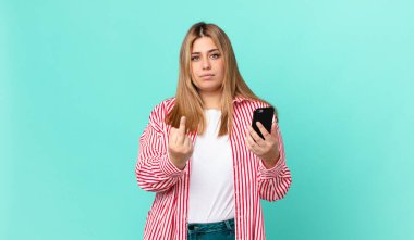 kıvrımlı, güzel, sarışın bir kadın kızgın, sinirli, asi ve agresif ve akıllı bir telefon tutuyor.