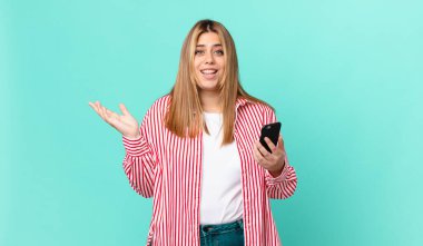 Kıvrımlı, güzel, sarışın bir kadın mutlu, bir çözüm ya da fikir bulduğunda şaşırmış ve elinde akıllı bir telefon tutuyor.