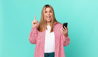 Güzel, kıvrımlı, sarışın bir kadın bir fikri fark ettikten sonra mutlu ve heyecanlı bir dahi gibi hissediyor ve elinde akıllı bir telefon tutuyor.