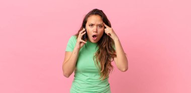 Genç, güzel bir kadın şaşırmış görünüyor, yeni bir düşünce, fikir ya da konsept buluyor ve elinde akıllı bir telefon tutuyor.