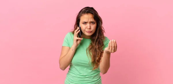 年轻漂亮的女人在做花言巧语或摆弄钱的姿势 让你付钱 并拿着智能手机 — 图库照片