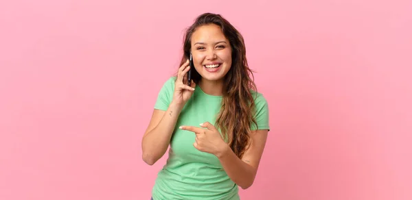 Młoda Ładna Kobieta Wygląda Podekscytowany Zaskoczony Wskazując Bok Trzymając Smartfon — Zdjęcie stockowe