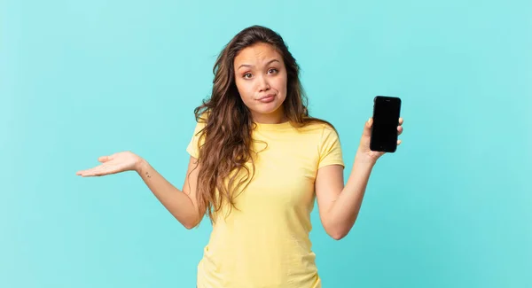 Joven Bonita Mujer Sintiéndose Desconcertado Confundido Dudando Sosteniendo Teléfono Inteligente —  Fotos de Stock