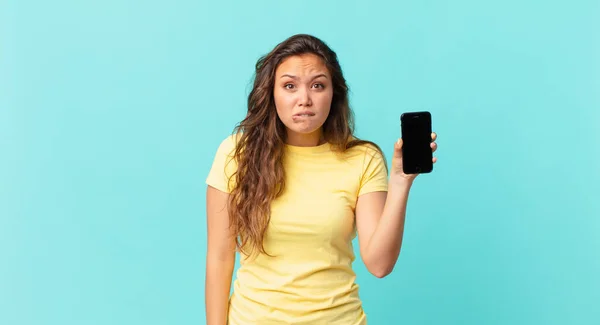 Młoda Ładna Kobieta Wygląda Zaskoczoną Zdezorientowaną Trzyma Smartfon — Zdjęcie stockowe
