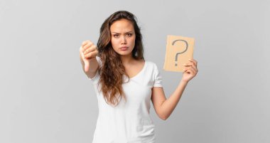 Genç, güzel bir kadın kendini kötü hissediyor, baş parmaklarını aşağı gösteriyor ve elinde bir soru işareti tutuyor.