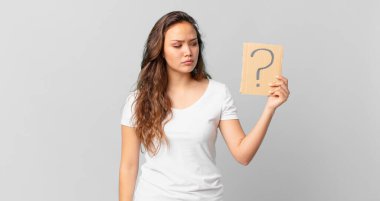 Genç, güzel bir kadın üzgün, üzgün ya da kızgın ve yan tarafa bakıyor ve elinde bir soru işareti var.