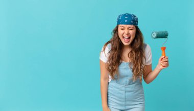 Genç ve güzel bir kadın agresif bir şekilde bağırıyor, çok kızgın görünüyor ve bir duvar boyuyor.