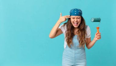 Genç ve güzel bir kadın mutsuz ve stresli görünüyor, intihar jesti silah işareti yapıyor ve duvar boyuyor.