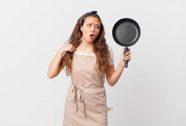 Genç, güzel bir kadın stresli, endişeli, yorgun ve hayal kırıklığına uğramış şef konsepti ve elinde bir tava tutuyor.