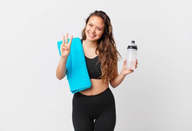 Genç, güzel bir bayan gülümsüyor ve arkadaş canlısı görünüyor, üç numarayı gösteriyor. fitness konsepti