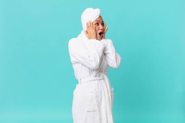 Genç ve güzel bir kadın mutlu, heyecanlı ve şaşırmış hissediyor ve duştan sonra banyo cübbesi giyiyor.