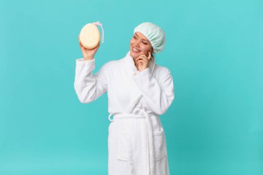 Genç, güzel bir kadın mutlu bir şekilde gülümsüyor ve hayal kuruyor ya da duştan sonra banyo cübbesi giyiyor.