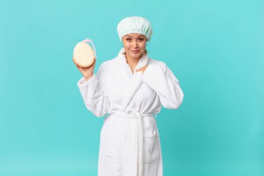 Genç ve güzel bir kadın kendini mutlu hissediyor ve heyecanla kendini işaret ediyor ve duştan sonra banyo cübbesi giyiyor.