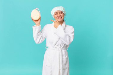 Genç, güzel bir kadın neşeyle gülümsüyor, mutlu hissediyor ve yan tarafı gösteriyor ve duştan sonra banyo cübbesi giyiyor.