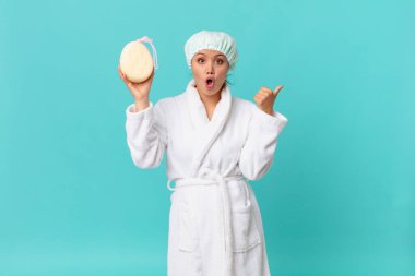 Genç ve güzel bir kadın inançsızlıktan şaşkına dönmüş ve duştan sonra banyo cübbesi giyiyor.