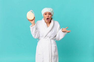 Genç ve güzel bir kadın inanılmaz bir sürprizle şaşkın ve şaşkın ve duştan sonra banyo cübbesi giyiyor.