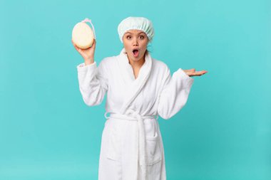 Genç ve güzel bir kadın şaşırmış ve şok olmuş görünüyor, çenesi düşmüş bir nesne tutuyor ve duştan sonra banyo cübbesi giyiyor.