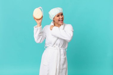 Genç ve güzel bir kadın kendini mutlu hissediyor ve bir meydan okumayla karşı karşıya ya da kutlama yapıyor ve duştan sonra bornoz giyiyor.