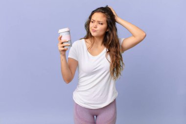Genç, güzel bir kadın kafası karışmış ve kafası karışmış hissediyor. Kafasını kaşıyor ve elinde kahve tutuyor.