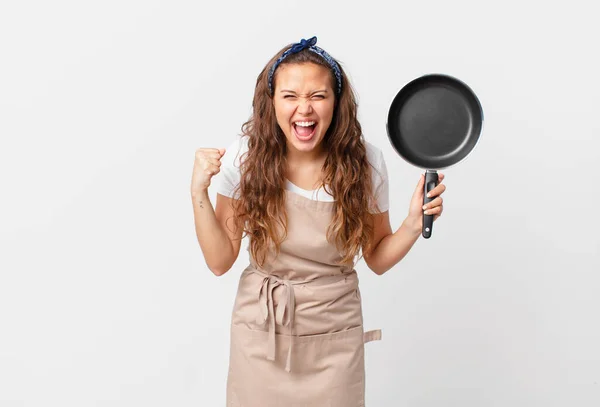 年轻漂亮的女人带着愤怒的表达厨师的概念大喊大叫 手里拿着一只锅 — 图库照片