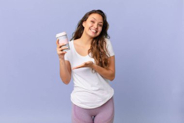 Genç, güzel bir kadın neşeyle gülümsüyor, mutlu hissediyor ve bir konsept gösteriyor ve elinde kahve tutuyor.