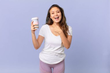 Genç ve güzel bir kadın heyecanlı ve şaşırmış görünüyor. Yan tarafı gösteriyor ve elinde kahve tutuyor.