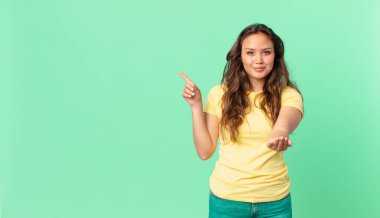 Genç ve güzel bir kadın mutlu bir şekilde gülümsüyor ve bir konsept sunuyor ve fotokopi alanını işaret ediyor.