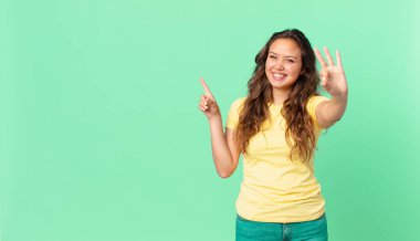Genç güzel bayan gülümsüyor ve arkadaş canlısı görünüyor, üç numarayı gösteriyor ve fotokopi alanını gösteriyor.