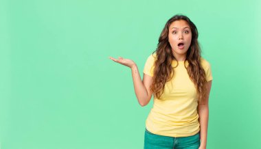 Genç ve güzel bir kadın şaşırmış ve şok olmuş görünüyor. Çenesi düşmüş, elinde bir nesne tutuyor ve kopyalama alanını işaret ediyor.