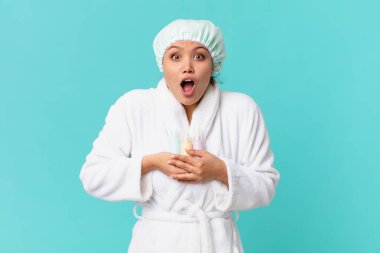 Bornoz giyen ve elinde temiz bir ürün şişesi tutan genç ve güzel bir kadın.