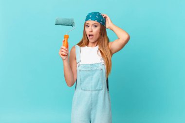 Güzel bir kadın kendini stresli, endişeli ya da korkmuş hissediyor. Elleri başının üstünde yeni bir ev duvarı boyuyor.