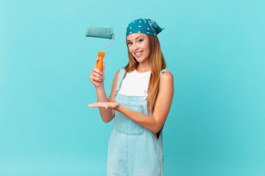 Güzel bir kadın neşeyle gülümsüyor, mutlu hissediyor ve yeni bir ev duvarı boyama konseptini gösteriyor.