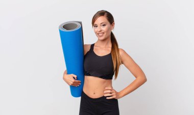 Güzel bir kadın mutlu bir şekilde gülümsüyor, eli kalçasında ve kendinden emin. yoga konsepti