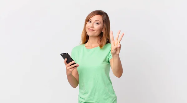 Pretty Woman Smiling Looking Friendly Showing Number Three Using Smartphone — Stock Photo, Image