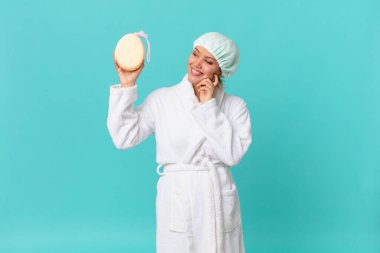 Genç, güzel bir kadın mutlu bir şekilde gülümsüyor ve hayal kuruyor ya da duştan sonra banyo cübbesi giyiyor.