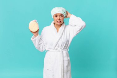 Genç, güzel bir kadın kendini stresli, endişeli ya da korkmuş hissediyor. Elleri başının üstünde ve duştan sonra banyo bornozu giyiyor.