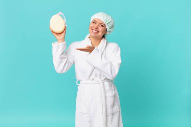 Genç, güzel bir kadın neşeyle gülümsüyor, mutlu hissediyor ve bir konsept gösteriyor ve duştan sonra banyo bornozu giyiyor.