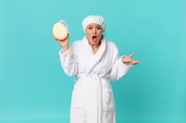 Genç ve güzel bir kadın inanılmaz bir sürprizle şaşkın ve şaşkın ve duştan sonra banyo cübbesi giyiyor.