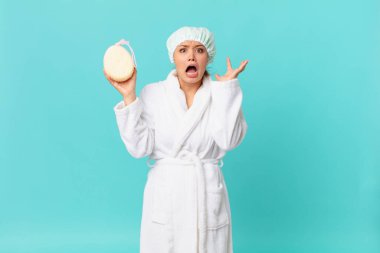 Genç ve güzel bir kadın ellerini havaya kaldırarak çığlık atıyor ve duştan sonra banyo cübbesi giyiyor.