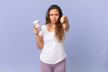 Genç, güzel bir kadın kendini kötü hissediyor, baş parmağını kaldırıyor ve elinde kahve tutuyor.