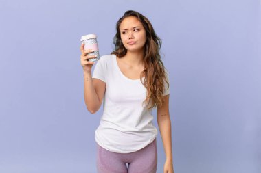 Genç, güzel bir kadın üzgün, üzgün ya da kızgın ve yana bakıyor ve elinde kahve tutuyor.