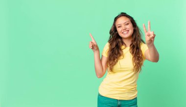 Genç ve güzel bir bayan gülümsüyor ve arkadaş canlısı görünüyor, iki numarayı gösteriyor ve fotokopi alanını işaret ediyor.