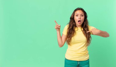 Genç ve güzel bir kadın ağzı açık, kendini işaret eden ve fotokopi alanını işaret eden şok olmuş ve şaşırmış görünüyor.